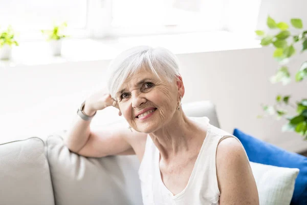 Porträtt av en glad senior kvinna sitter i soffan i vardagsrummet — Stockfoto