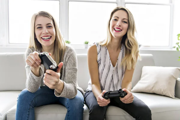 两个美丽的女孩坐在沙发上与游戏控制器 — 图库照片