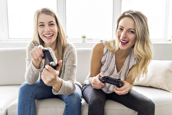 To vakre, unge kvinner som sitter på sofaen med spillkontroll – stockfoto