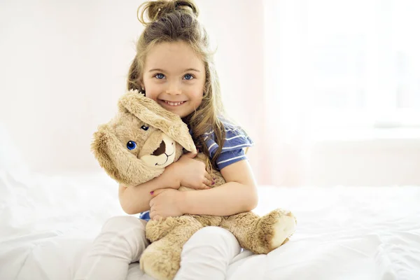 Doce menina está abraçando um ursinho de pelúcia em sua cama em casa — Fotografia de Stock