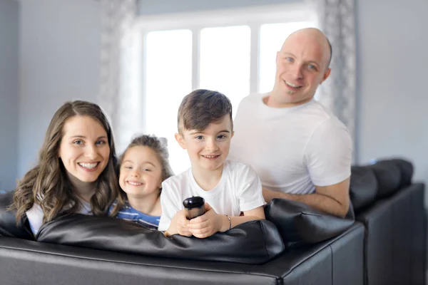 Família sentada na sala de estar com controle remoto sorrindo — Fotografia de Stock