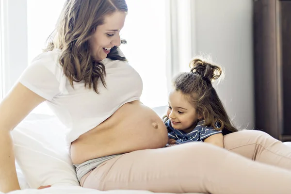 Pregnant woman with her daughter on bedroom together — Stock Photo, Image