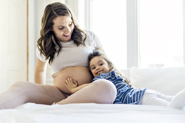 Zwangere vrouw met haar dochter op de slaapkamer samen — Stockfoto