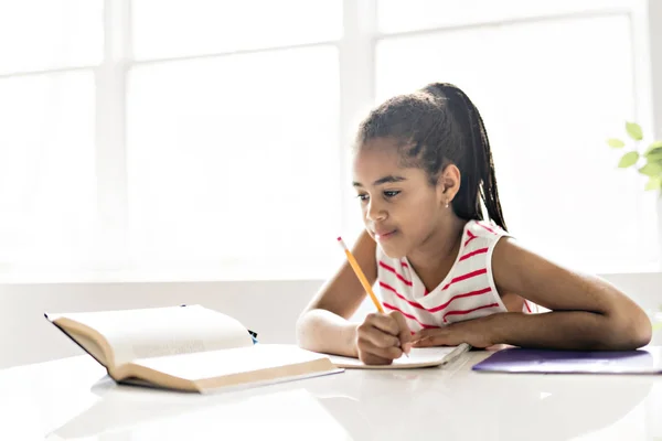 Милая черная девушка делает домашнее задание дома — стоковое фото