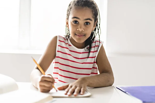 Милая черная девушка делает домашнее задание дома — стоковое фото