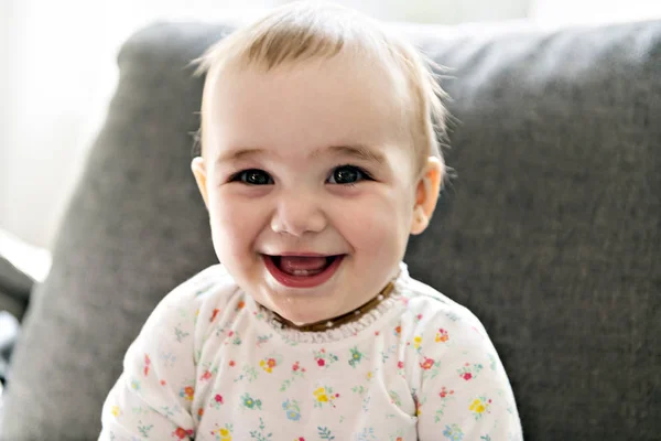 Un bambino sorridente su un divano grigio — Foto Stock