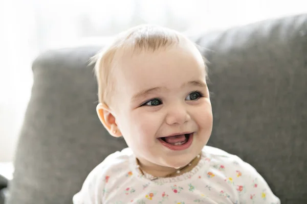 Un bambino sorridente su un divano grigio — Foto Stock