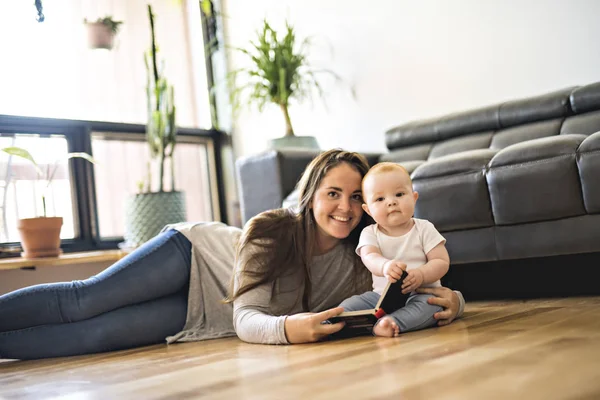 Gyönyörű nő a baba, és egy könyvet a nappaliban — Stock Fotó