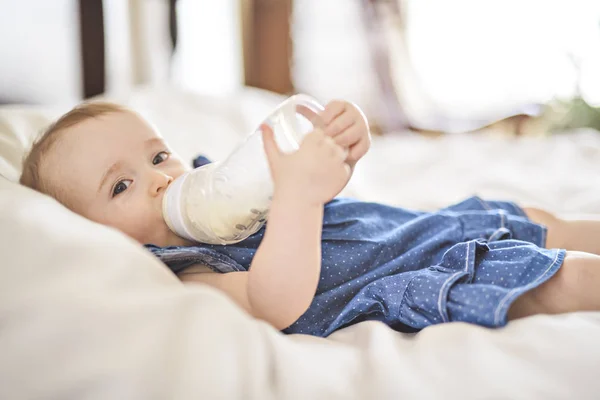 Hübsches kleines Mädchen trinkt Wasser aus Flasche, die auf Bett liegt — Stockfoto