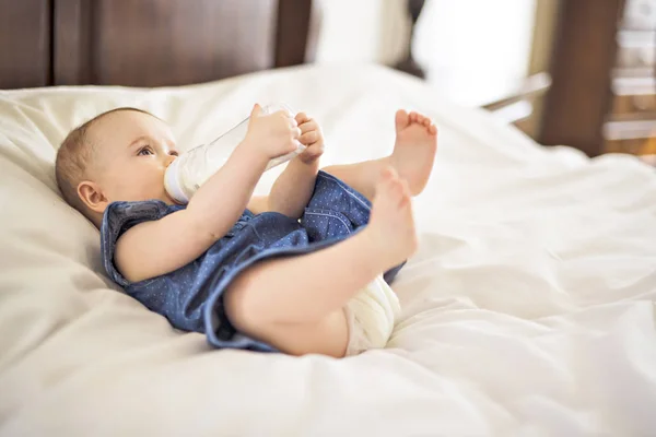 Jolie petite fille boit de l'eau du biberon couché sur le lit — Photo