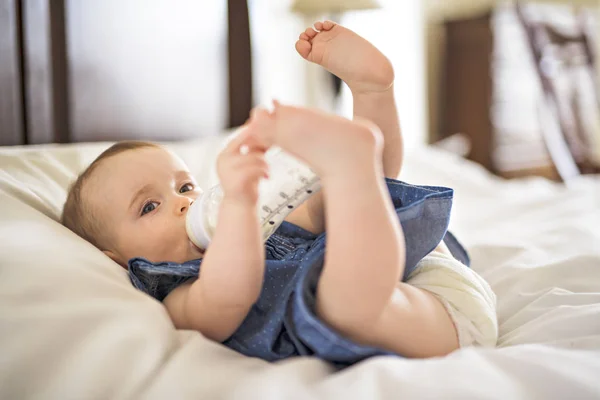 Красивая малышка пьет воду из бутылки, лежащей на кровати — стоковое фото