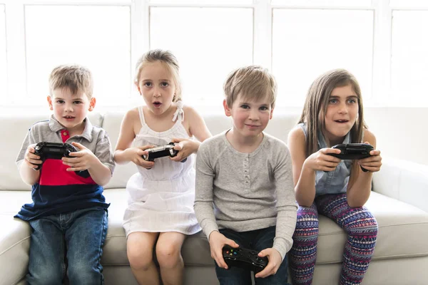 Cheerful kids are sitting together on sofa at home play video game — Stock Photo, Image