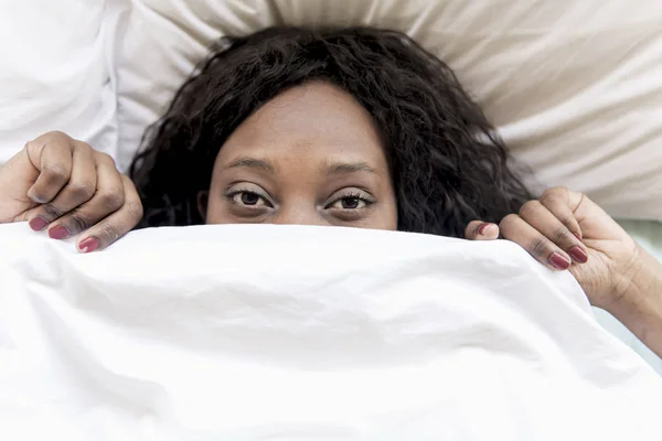 Uma mulher negra com medo debaixo da cama cobertor — Fotografia de Stock