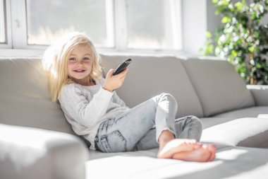 4 years old child watching tv laying down on the sofa at home alone clipart