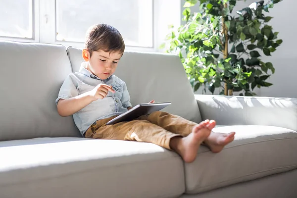 小さな男の子とデジタルタブレットソファの上に座って、ホームインテリアの背景に — ストック写真