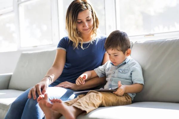 Little boy with digital tablet sitting on sofa, on home interior background with mom — Stock Photo, Image