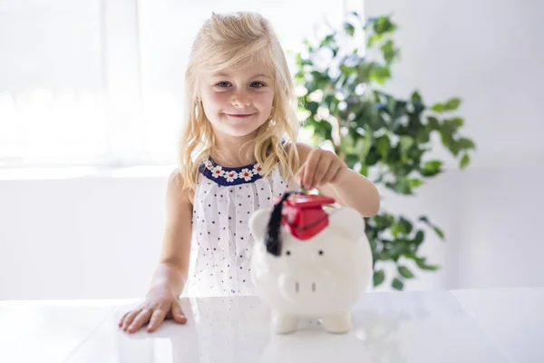 Usměvavá holčička s prasátko a peníze doma — Stock fotografie