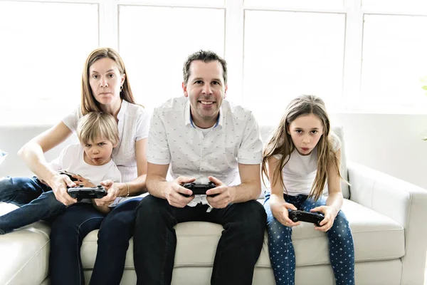 Family of four having fun on the sofa at home play video game