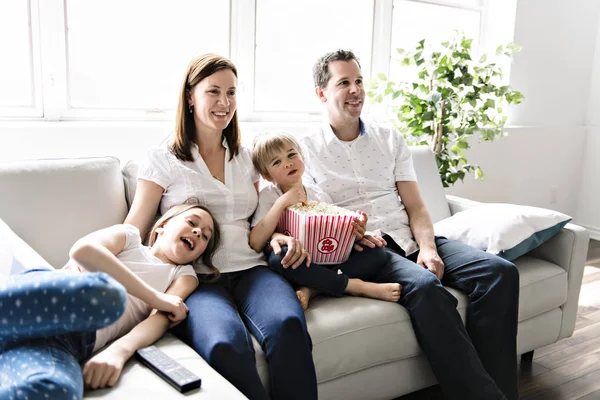 Сім'я з чотирьох розважається на дивані вдома дивитися фільм з попкорном — стокове фото