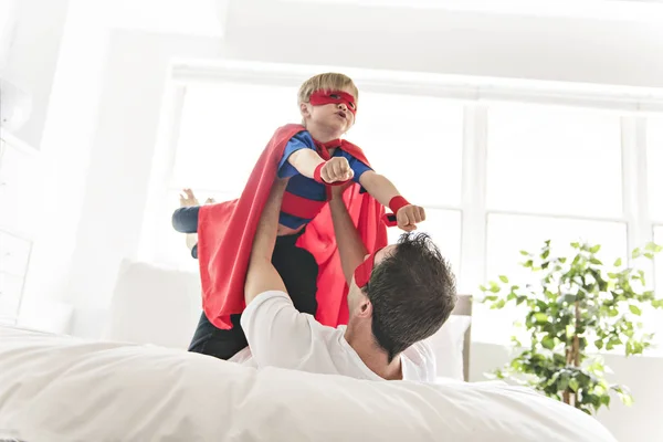 Pai e filho jogar super-heróis na cama em casa — Fotografia de Stock