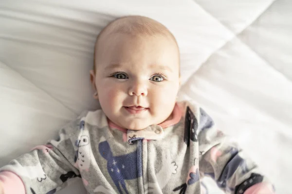Una bambina carina su un letto bianco a casa — Foto Stock