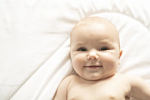 Una linda niña en una cama blanca en casa — Foto de Stock