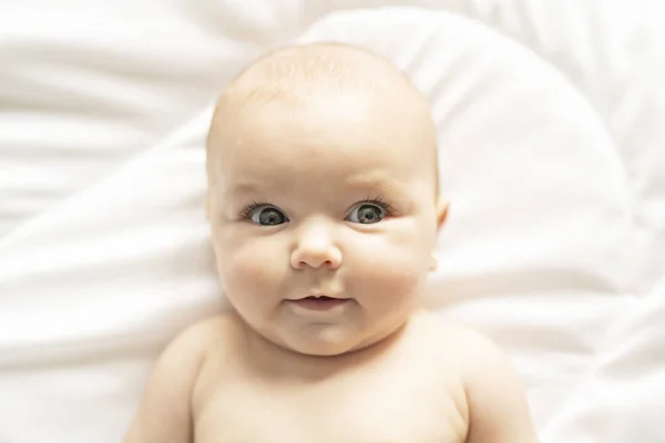 Una linda niña en una cama blanca en casa — Foto de Stock