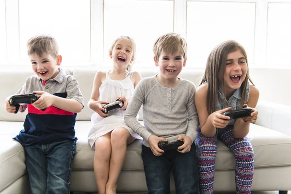 Веселые дети сидят вместе на диване в домашней видеоигре — стоковое фото