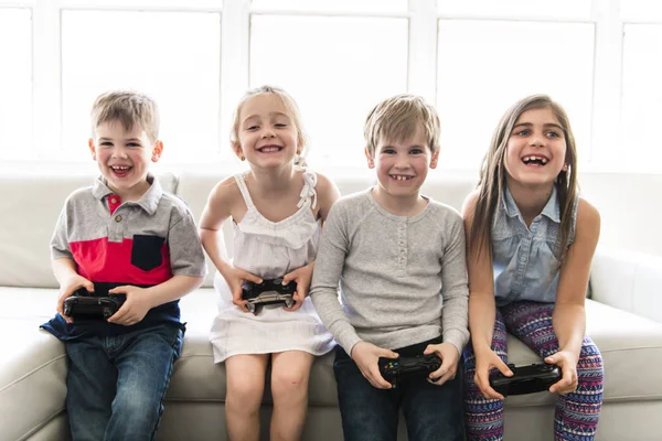 I bambini allegri sono seduti insieme sul divano a casa a giocare ai videogiochi — Foto Stock