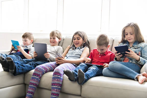 グループの子供に座ってソファ自宅とのタブレット、ビデオゲーム — ストック写真