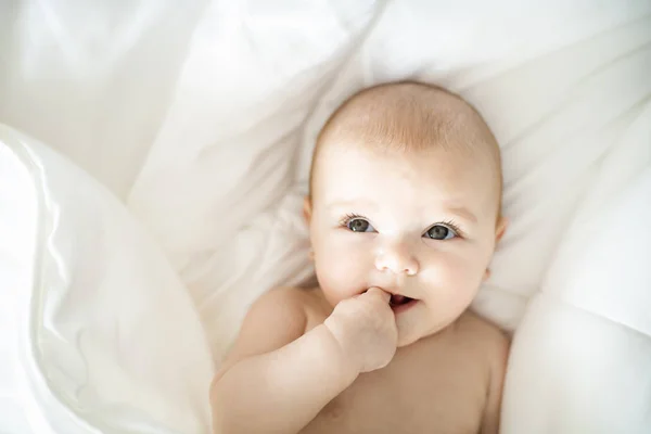 Um bebê bonito menina em uma cama branca em casa — Fotografia de Stock