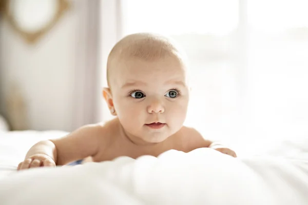 Um bebê bonito menina em uma cama branca em casa — Fotografia de Stock