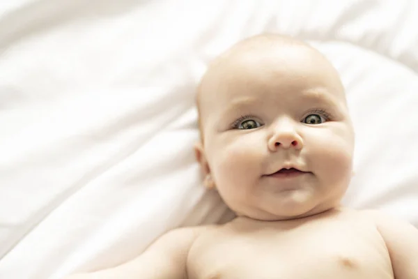 Una linda niña en una cama blanca en casa — Foto de Stock