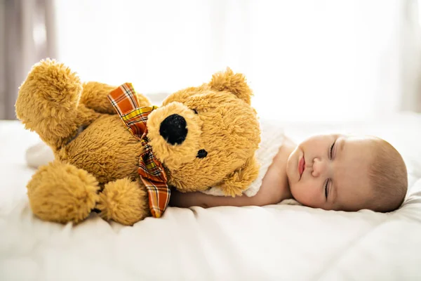 A 4 month baby sleeping on a white bed at home with bear — Stock Photo, Image