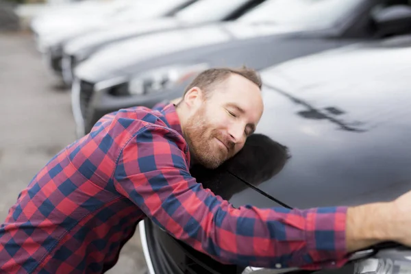 Een gelukkige jongeman knuffelt zijn auto buiten garage winkel — Stockfoto