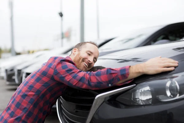 Een gelukkige jongeman knuffelt zijn auto buiten garage winkel — Stockfoto