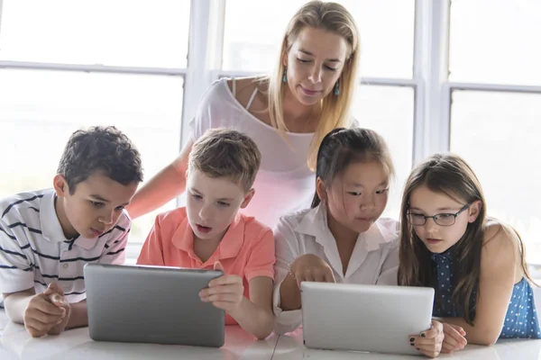 Ребенок с технологическим планшетом и ноутбуком в классе учитель на заднем плане — стоковое фото