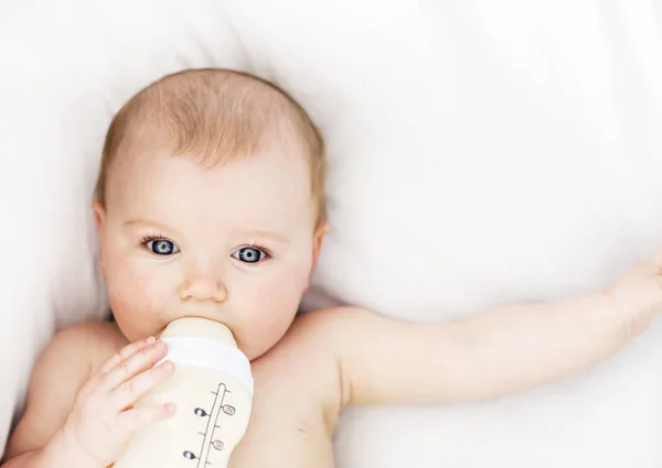 Jolie petite fille boit de l'eau du biberon couché sur le lit. Couche portée enfant dans la chambre d'enfant . — Photo