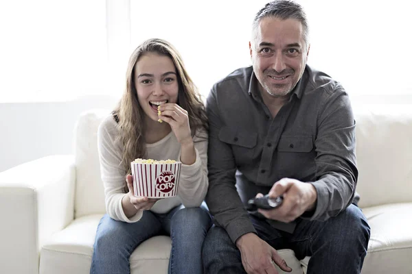 Retrato de un joven y su hija viendo la televisión mientras comen palomitas de maíz en el sofá — Foto de Stock