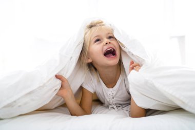 A Cheerful little girl in bed having fun clipart