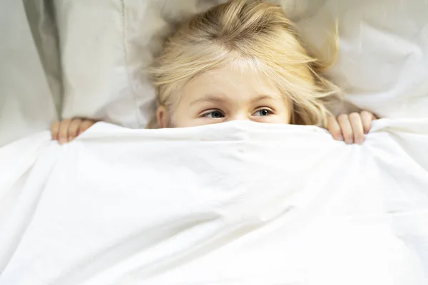 Ένα μικρό κορίτσι στο κρεβάτι κάτω από τα σκεπάσματα — Φωτογραφία Αρχείου