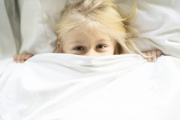 Une petite fille au lit sous les couvertures — Photo