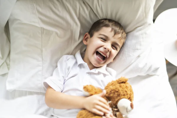 Uma criança deitada na cama com um urso de pelúcia — Fotografia de Stock