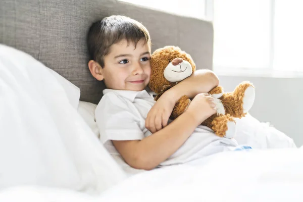 Uma criança deitada na cama com um ursinho de pelúcia — Fotografia de Stock