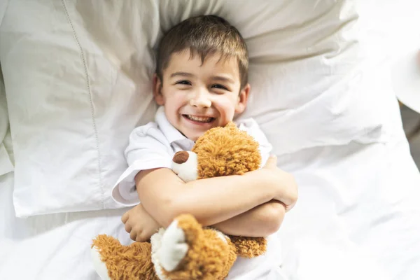 Uma criança deitada na cama com um ursinho de pelúcia — Fotografia de Stock