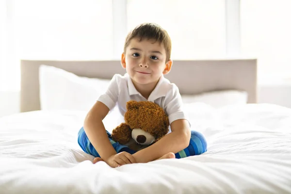 Uma criança senta-se na cama com um ursinho de pelúcia — Fotografia de Stock