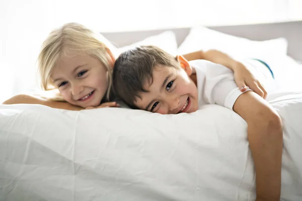 Um retrato de irmãos felizes deitados debaixo do cobertor na cama no quarto em casa — Fotografia de Stock
