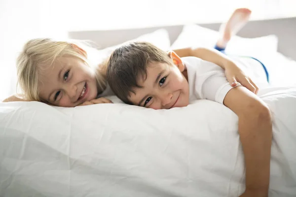 Портрет счастливых братьев и сестер, лежащих под одеялом на кровати в спальне дома — стоковое фото