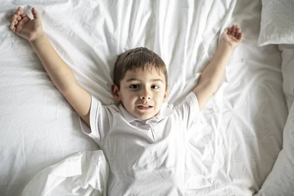 Un niñito acostado en la cama con manta blanca — Foto de Stock