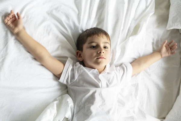 Een kleine jongen lag op het bed met witte deken — Stockfoto